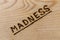 The word madness handwritten with woodburner on flat plywood surface in flat lay directly above view with diagonal composition