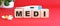 The word MEDI is made of wooden cubes on a red background. Medical concept