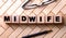 The word MIDWIFE is written on wooden cubes on a wooden background next to a pen and glasses