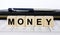A word Money written in a wooden cube with a pen and purse