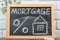 The word mortgage on a black chalk board, a drawing of the symbol of interest and house