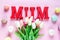 Word Mum from red letters and tender tulips, macaroons on pink background. Mothers day decoration concept. Top view, flat lay