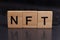 word NFT, non-fungible token made from wooden blocks on a laptop. The concept of earning on NFT