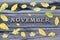 Word November, wooden letters. Frame of yellow leaves, wooden background