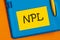 The word NPL is written in black marker on the yellow paper for notes. NPL - Non Performing Loan acronym, business concept