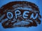 Word Open hand written on roast ground coffee on a blue background top view. Can be used as creative Open sign for coffee shops, c