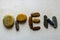 Word: OPEN, written using colored stones on white sand