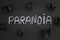 The word Paranoia on a black background with black crumpled paper balls around it