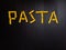Word pasta made of yellow dry pasta on the black background. Five letters made from pasta.
