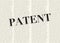 The word PATENT written and highlighted in front of blurred text columns on background of light yellow color