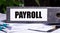 The word PAYROLL is written on a gray file folder next to documents. Business concept