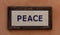 Word peace made from cubes. Mosaic pattern, wooden frame, warm brown background. Close up view.