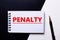 The word PENALTY is written on a black and white background near a pen. Financial concept
