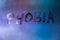 the word phobia handwritten on wet foggy window glass surface with blue background light