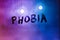 the word phobia handwritten on wet foggy window glass surface with purple-blue background light