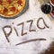 The word Pizza written in flour with various ingredients