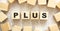 The word PLUS consists of wooden cubes with letters, top view on a light background