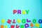 Word PRAY made of colorful letters on blue background.