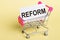The word REFORM on a card, on a yellow background with a shopping trolley