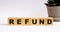 The word REFUND on wooden cubes on a light background near a flower in a pot. Defocus