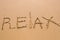 Word Relax hand written in the sand. Close up sand texture on beach in summer. Vacation, holiday concept