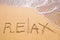 Word Relax hand written in the sand with a sea wave. Close up sand texture on beach in summer