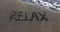 Word relax is written by hand on sandy beach