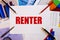 The word RENTER is written on a white table near graphs, pencils and pens. Financial concept