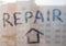 The word `repair` is written with a finger on a dirty, dusty glass against the background of an apartment building