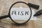 The word `risk` through a magnifier, written in black marker. Close-up. Wood background.