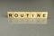 Word routine is made up of square wooden letters on a gray background