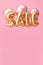 Word SALE made of golden inflatable balloons on pink background. Helium balloons gold foil forming word sale. Discount and