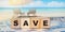 Word SAVE on wood cubes on mosaic border of swimming pool. Budget travel concept