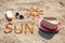 Word and shape of sun, sunglasses, sun lotion and straw hat on sand at beach, summer time