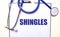 The word SHINGLES is written on a white sheet near the stethoscope. Medical concept