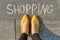Word shopping written on gray sidewalk with women legs, top view