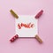 Word smile handwritten with watercolor in calligraphy style, miniature clothespins on a pink background. Flat lay