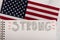 The word strong hand written on white paper American stars and stripes flag in the background