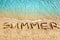 Word SUMMER written on yellow sand, blue sea water wave, white foam top view close up, handwriting letters text, summer vacations