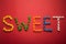 Word sweet from colorful candies on red paper background.