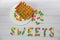 Word sweets written by round colorful chocolate button candies and fresh fried viennese waffles on white wooden table background.