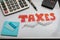 The word TAXES in red on a dry erase board office supplies calculators posted notes and pen