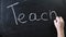 The word `teach` written on a black chalkboard. The sign is written on a chalk board. Male hand draws in chalk on a