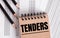 The word TENDERS is written on the brown notebook. Nearby pencils