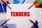 The word TENDERS is written on a white background near colored graphs, pens and pencils. Business concept