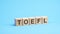 word TOEFL made with wood building blocks. text is written in black letters, blue background