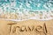 Word TRAVEL written on yellow sand, blue sea water wave, white foam top view close up, handwriting letters text, summer vacation