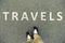 Word travels written on an asphalt road. Top view of the legs an