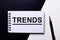 The word TREND is written on a black and white background on a piece of paper near the pen. Marketing concept