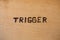 The word trigger handwritten on flat bare plywood surface with woodburner